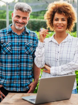 Homem e mulher ao lado de notebook no meio de plantação